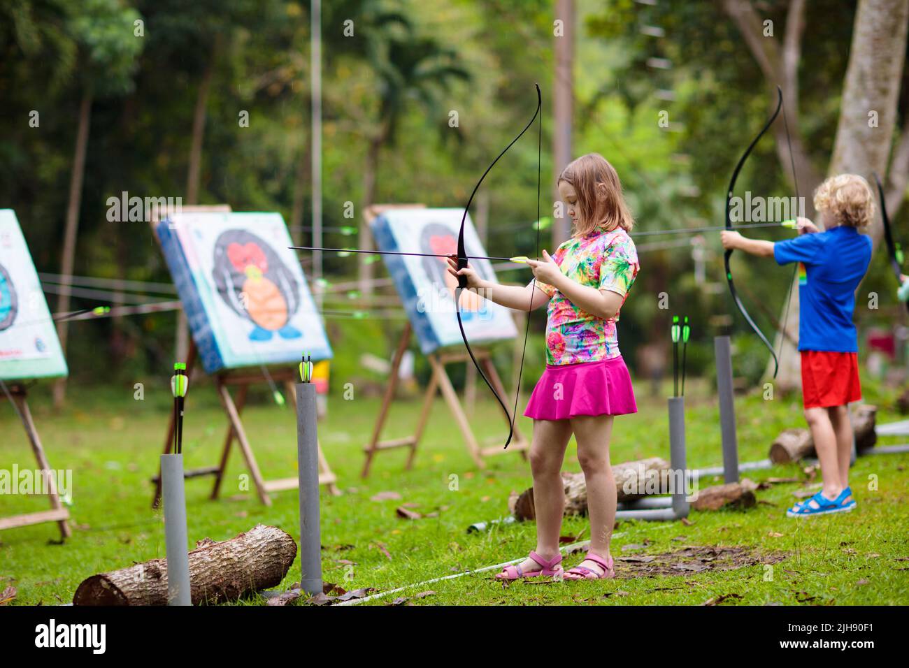 Archery for child. Little girl with bow and arrow. Kids shoot on tropical island. Target on