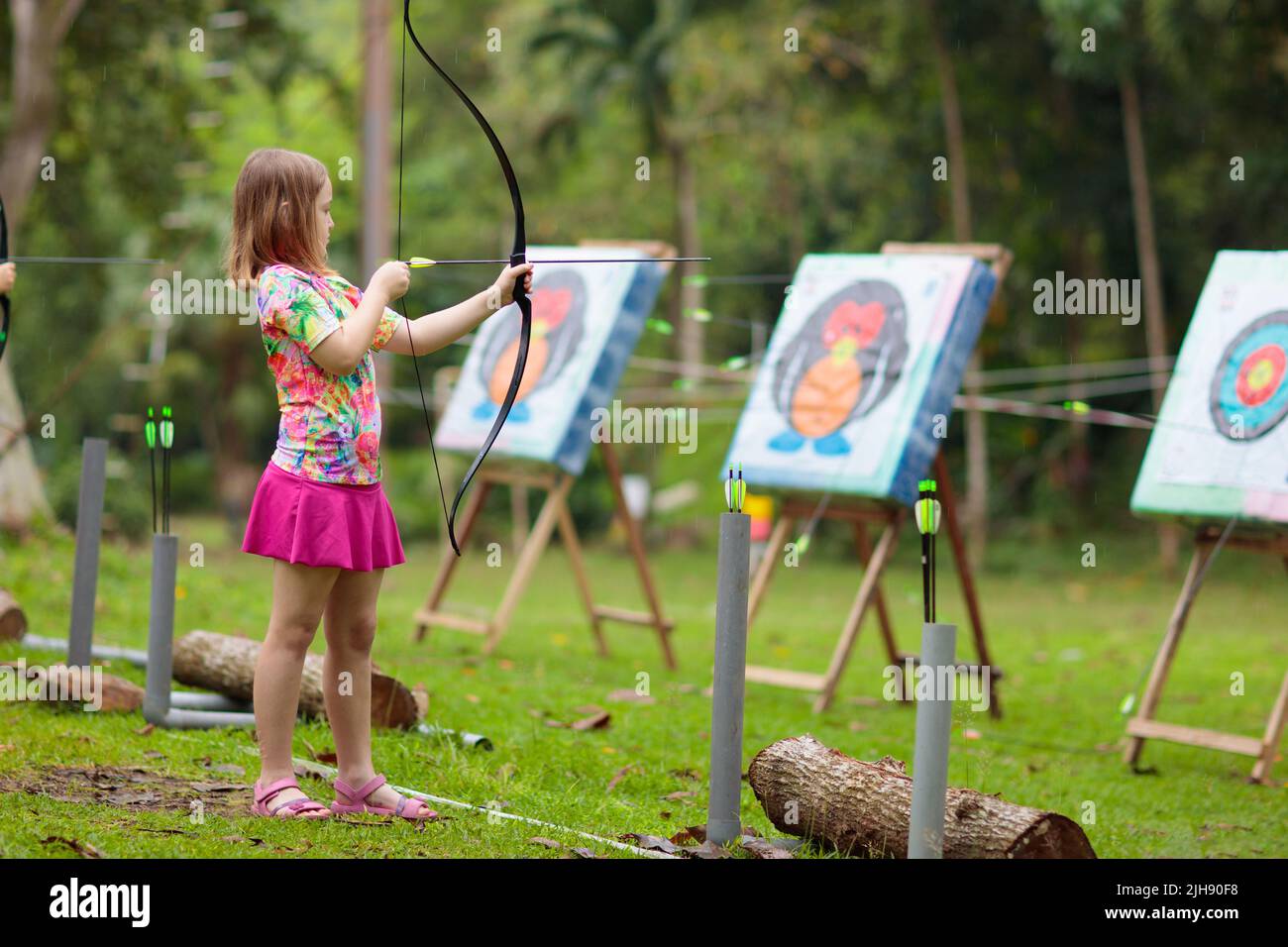 Archery for child. Little girl with bow and arrow. Kids shoot on tropical island. Target on
