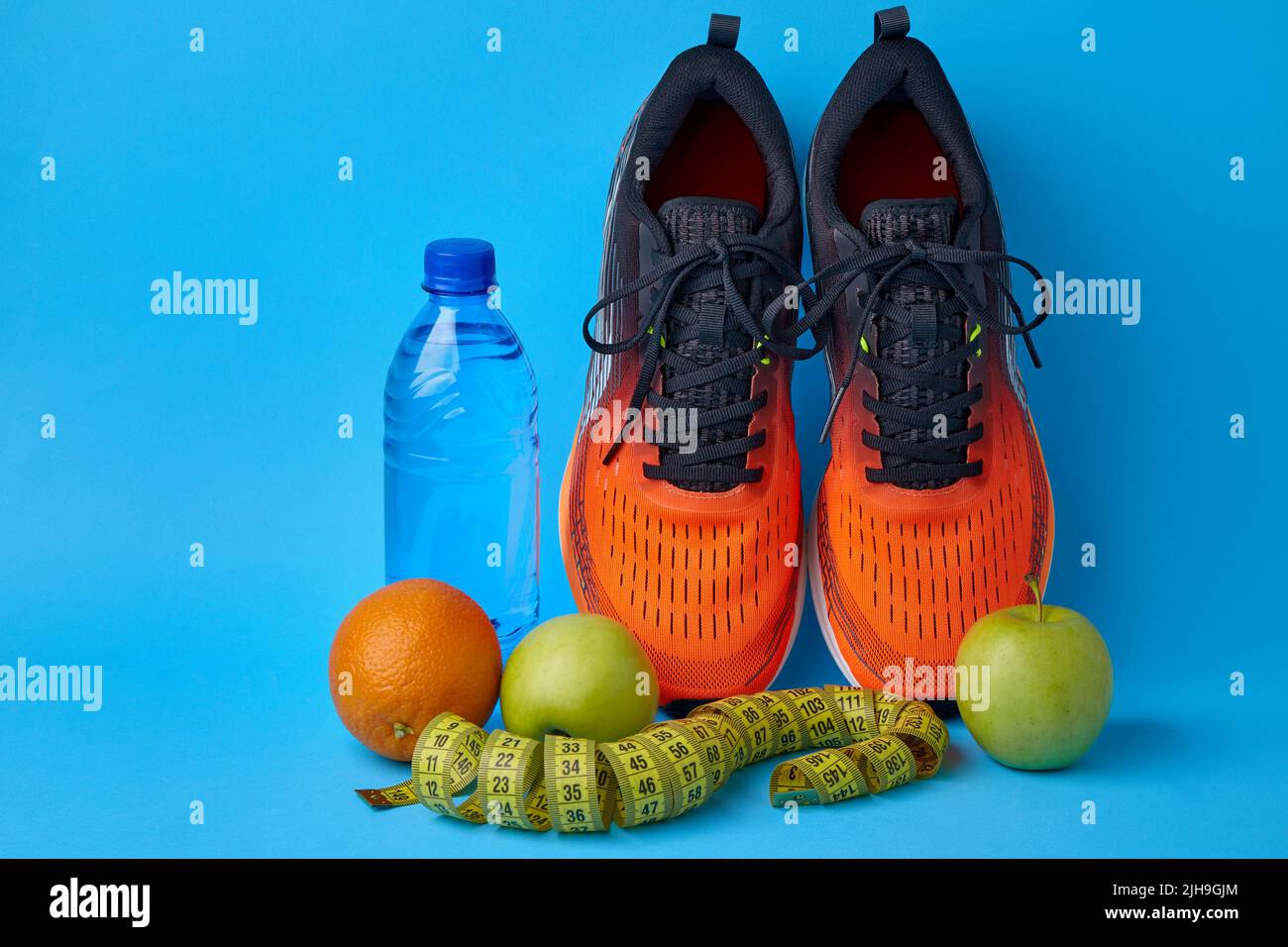 Orange sneakers, measuring tape, water bottle and fruits apples and