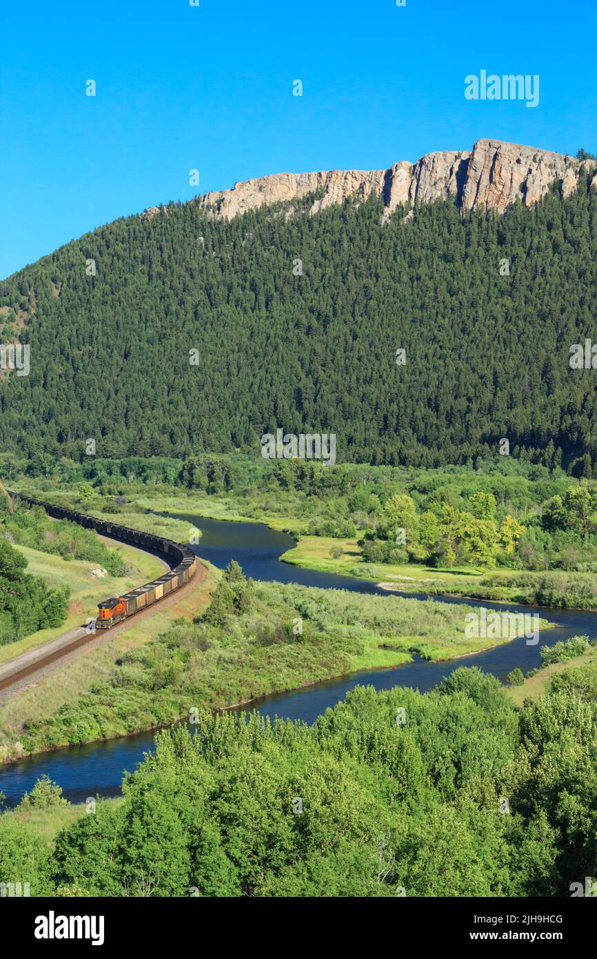 train on railroad tracks below high cliffs along the clark fork river valley near drummond, montana Stock Photo