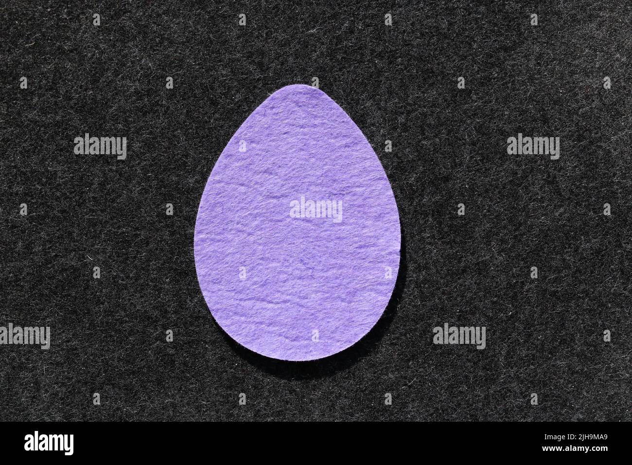 Single purple felt egg shape against dark grey felt background Stock Photo
