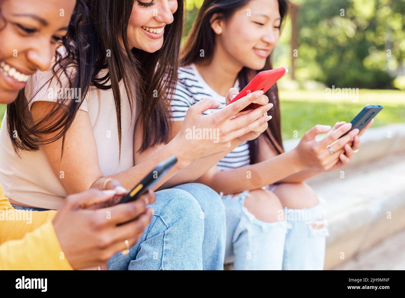 Happy young multiracial female friends using smart mobile phone together outdoor Stock Photo