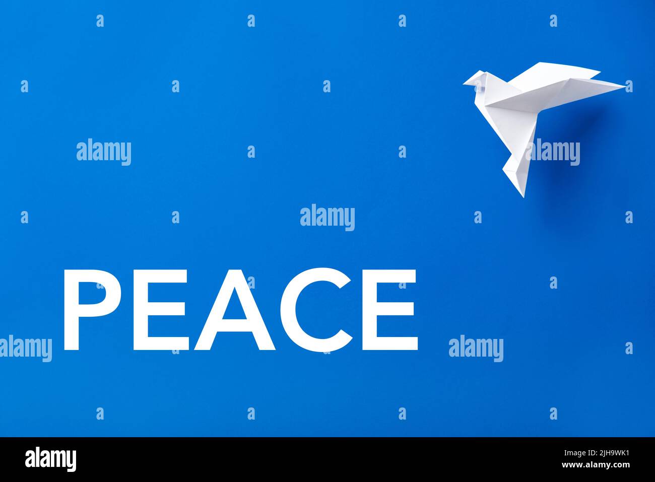 Word Peace in white letters on a blue background next to a flying white paper dove, symbol of peace. Stock Photo