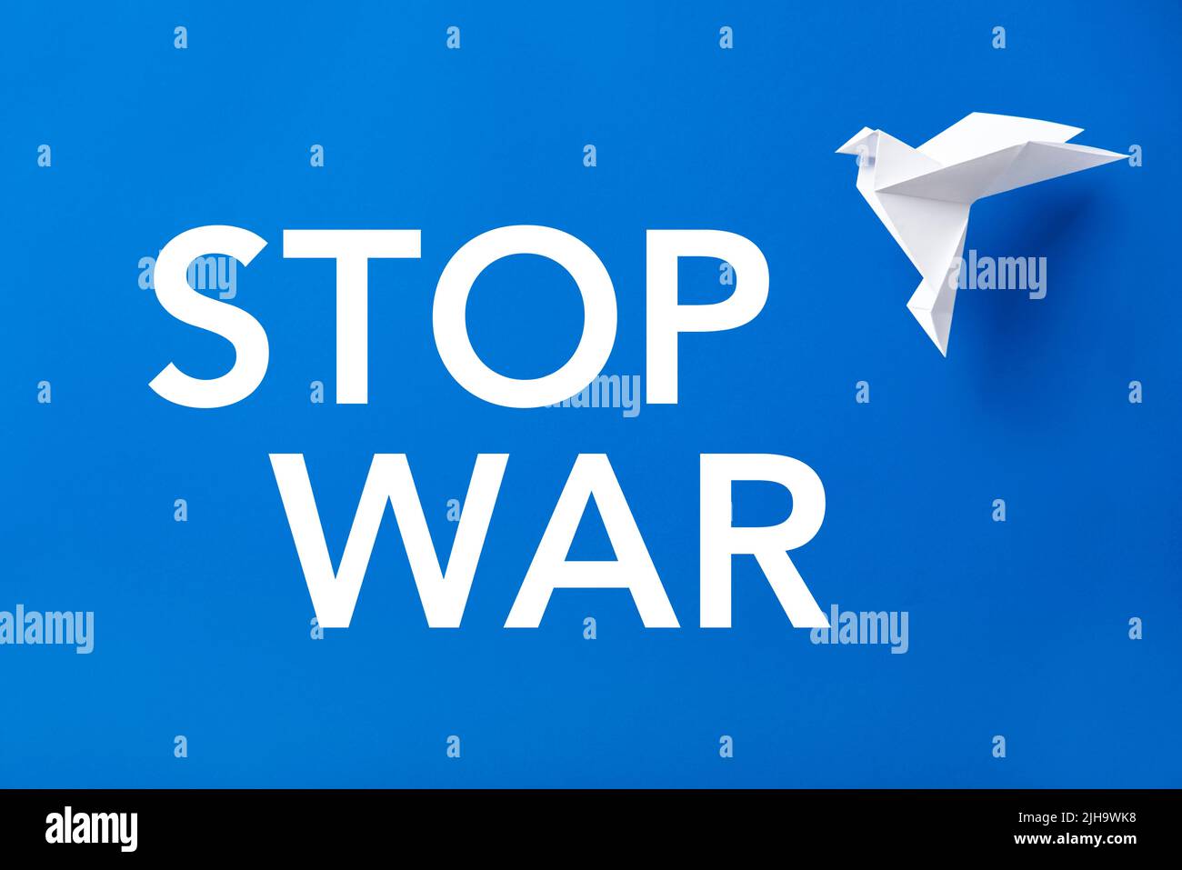 Text Stop war in white letters on a blue background next to a flying white paper dove, symbol of peace. Stock Photo