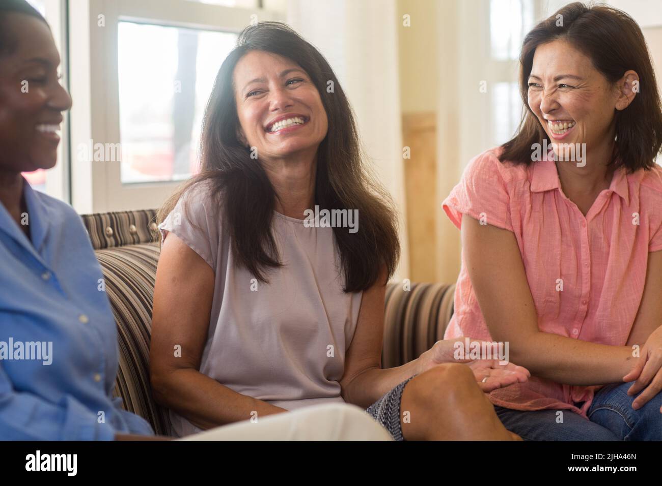 Friends laughing and talking sitting at home on the sofa Stock Photo