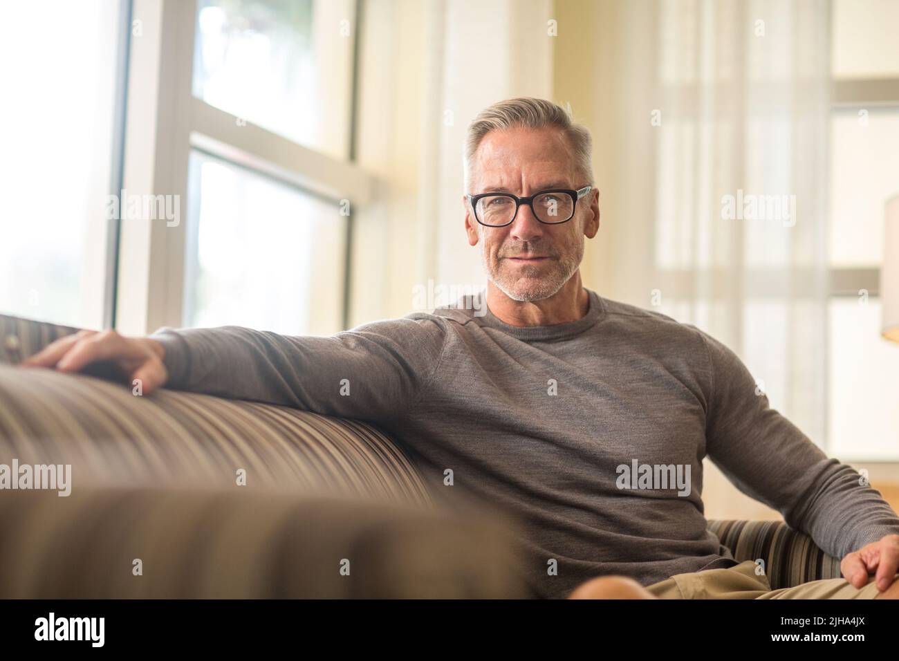 Handsome older man sitting on a sofa. Stock Photo