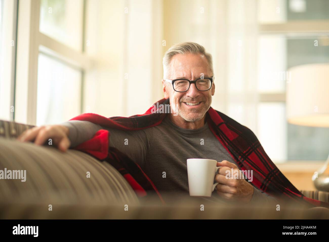 Mature man sitting on a sofa drinking coffee. Stock Photo