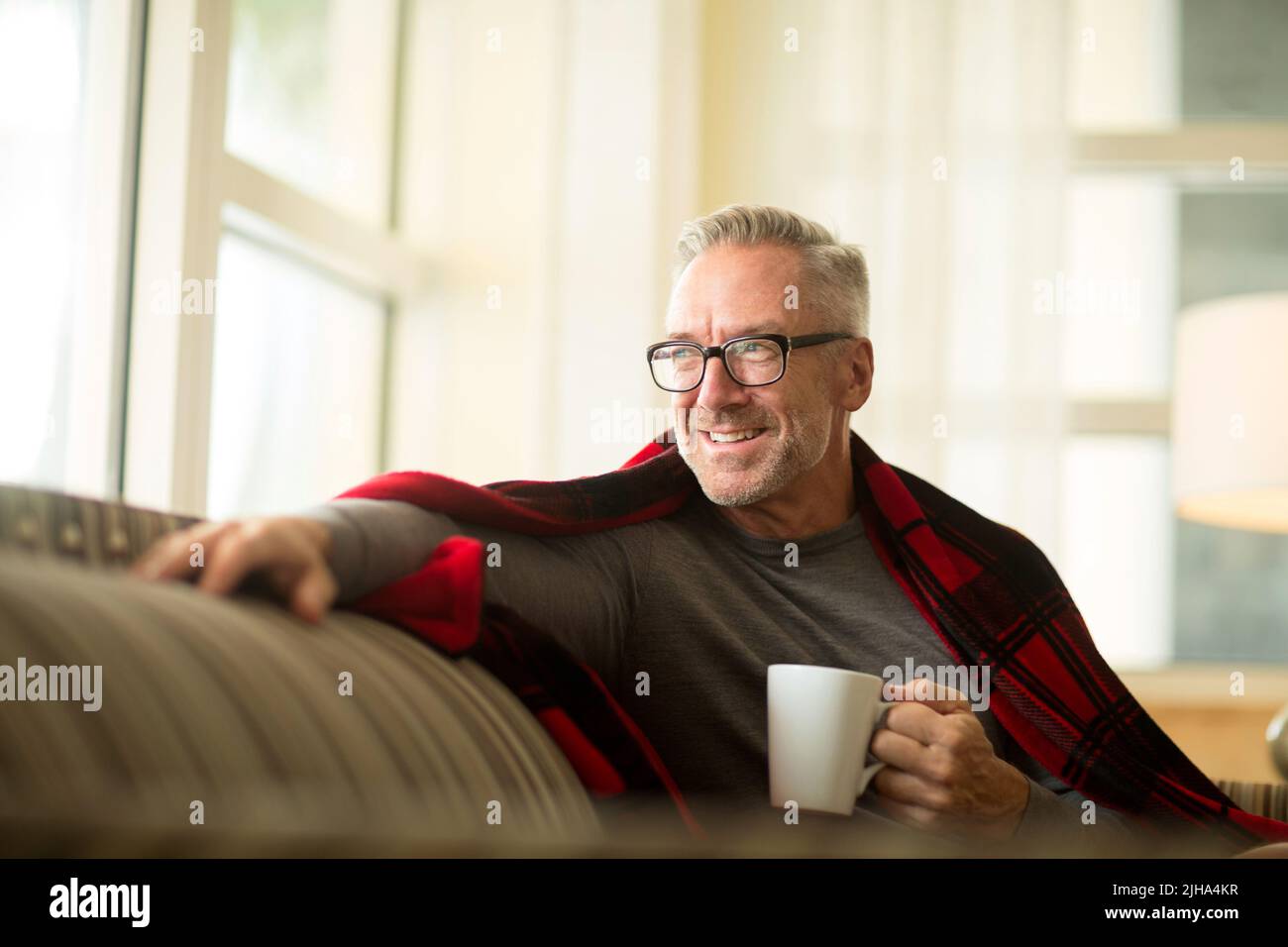 Mature man sitting on a sofa drinking coffee. Stock Photo