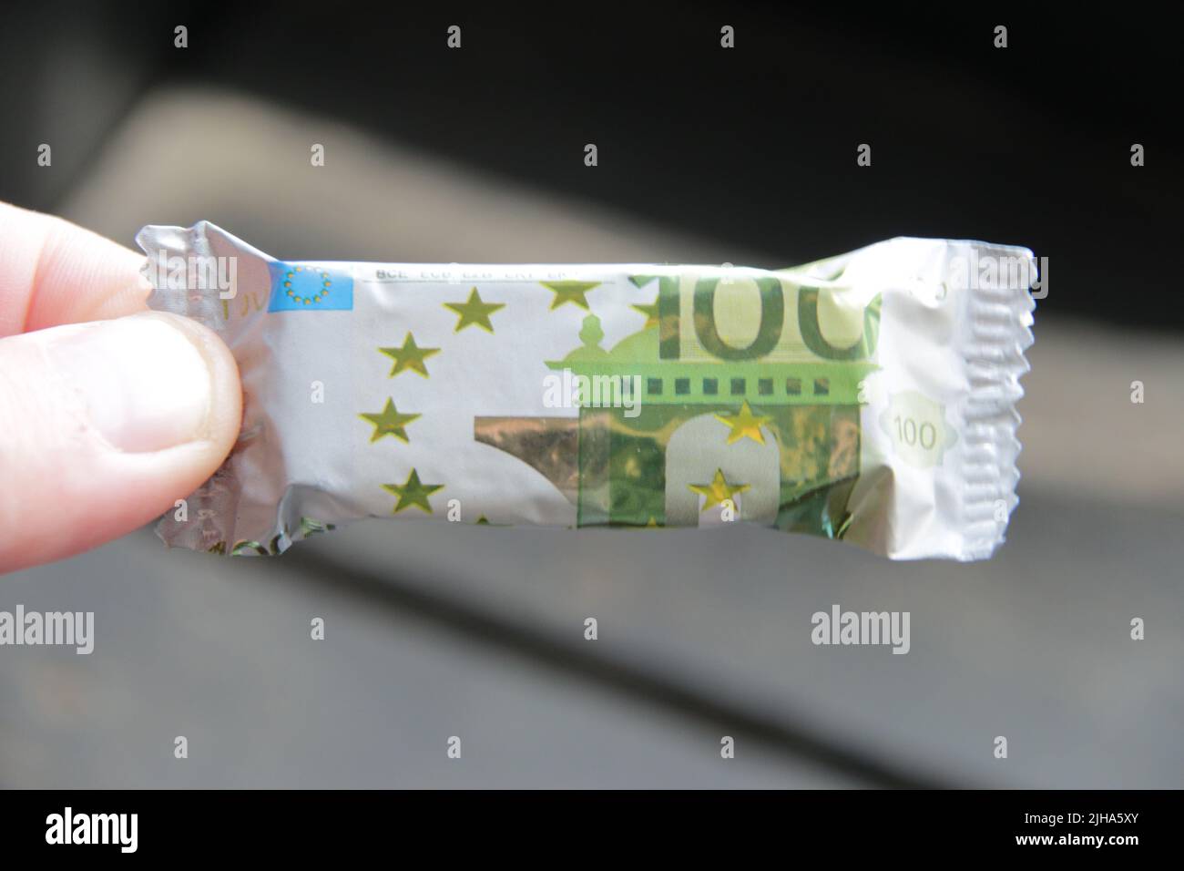 A hand holds a candy with a wrapper in the form of a one hundred euro banknote Stock Photo