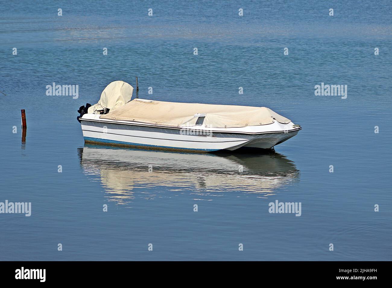 KANONI, CORFU, GREECE - SEPTEMBER 13, 2017 fishing boat moored to a stick with cover on in still clear blue water with reflections Stock Photo