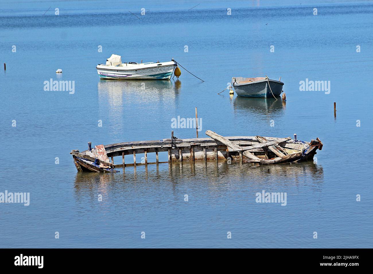 KANONI, CORFU, GREECE - SEPTEMBER 13, 2017 rotting skeleton of a traditional wooden row boat in clear blue water with modern boats in the background Stock Photo
