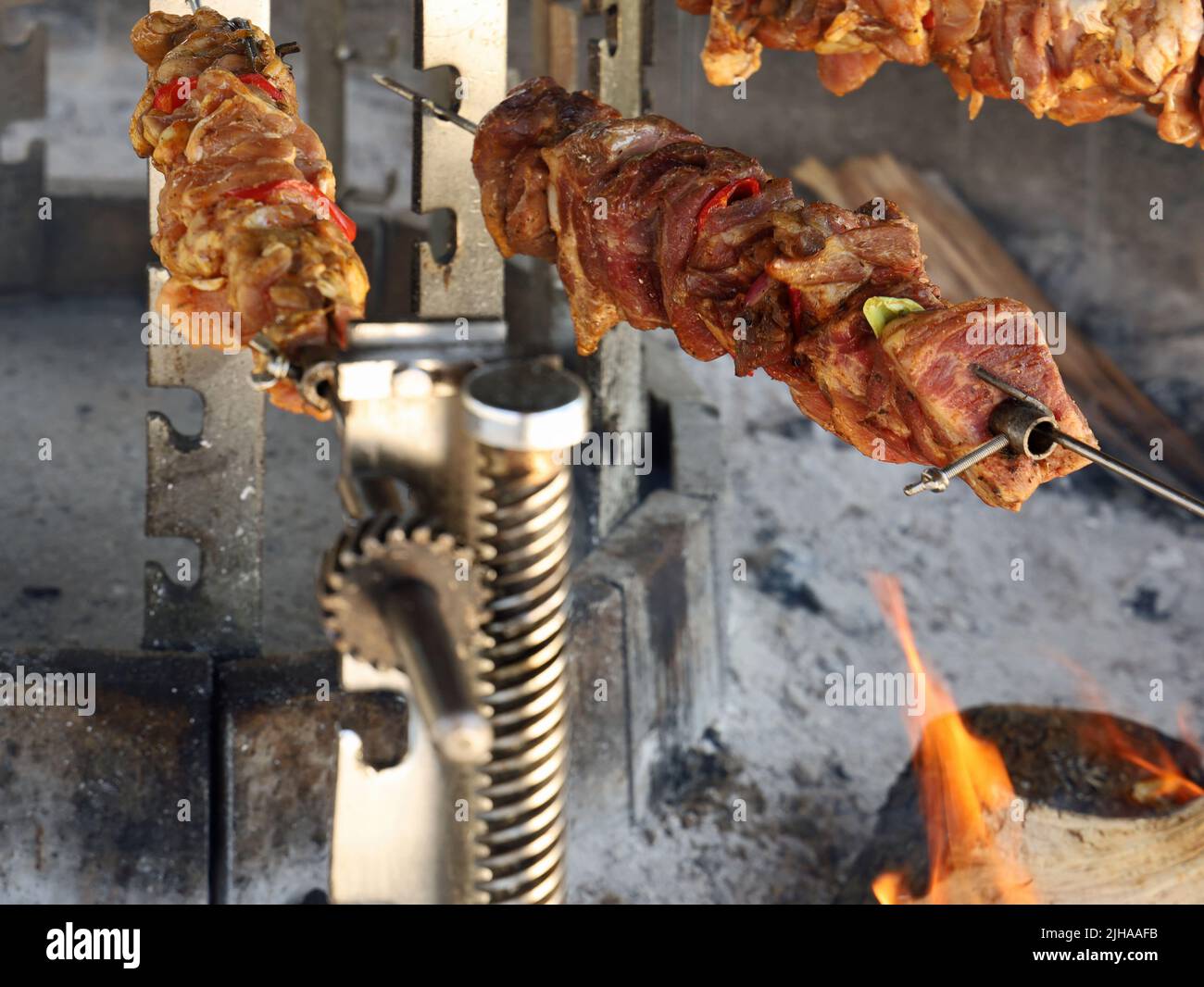 close up of seasoned cuts of meat on a rotisserie rolling over a wooden fire Stock Photo