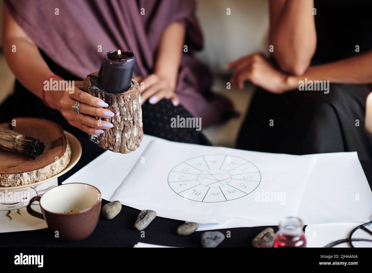 Sorceress burning black candle over natal card of client to ward off