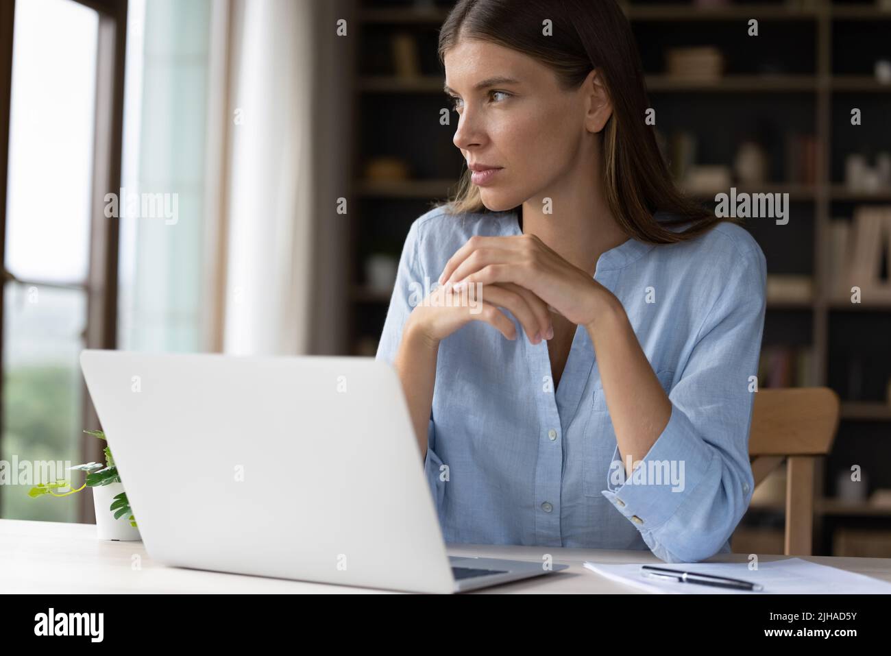 Thoughtful businesswoman sit at desk with laptop looking into distance Stock Photo