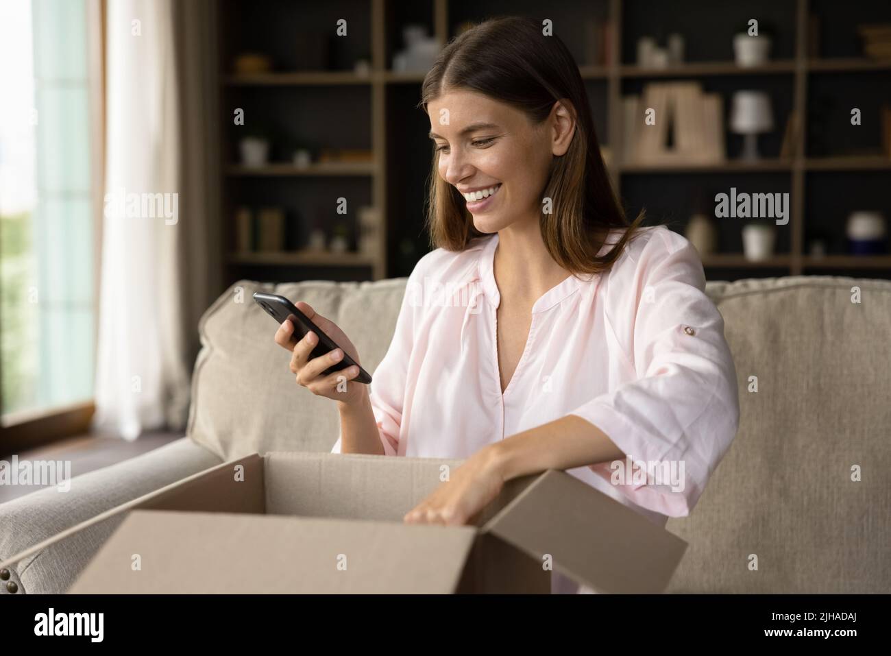 Woman unbox parcel, check order in phone use ecommerce application Stock Photo
