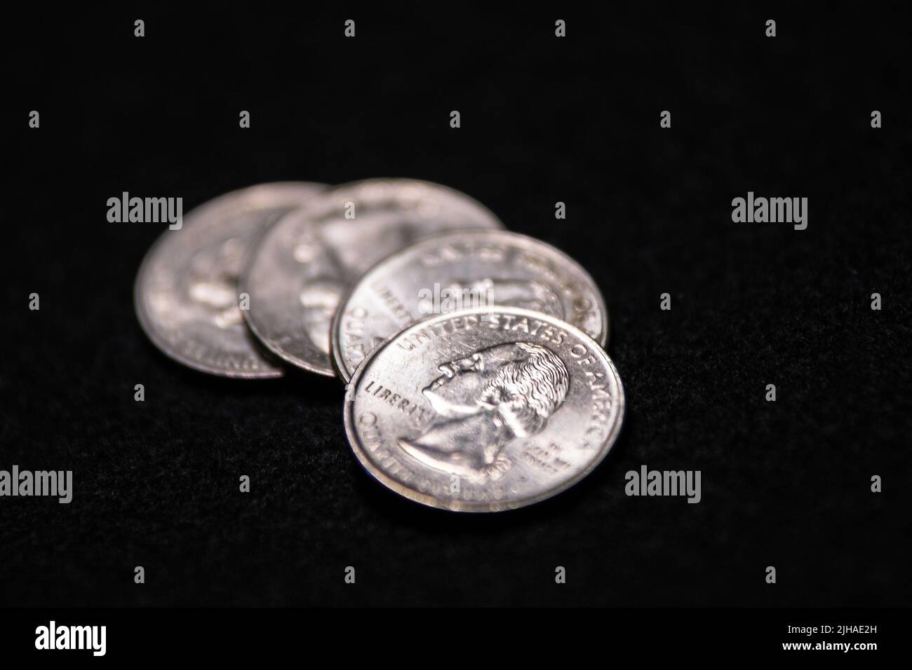 Shallow focus on one United States Quarter loosely stacked on three others that are out-of-focus on a black felt background with negative space. Stock Photo