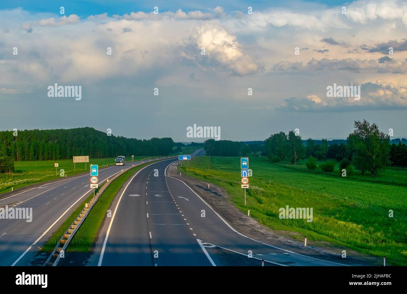 view of a summer paved highway with road signs among hills and a green ...