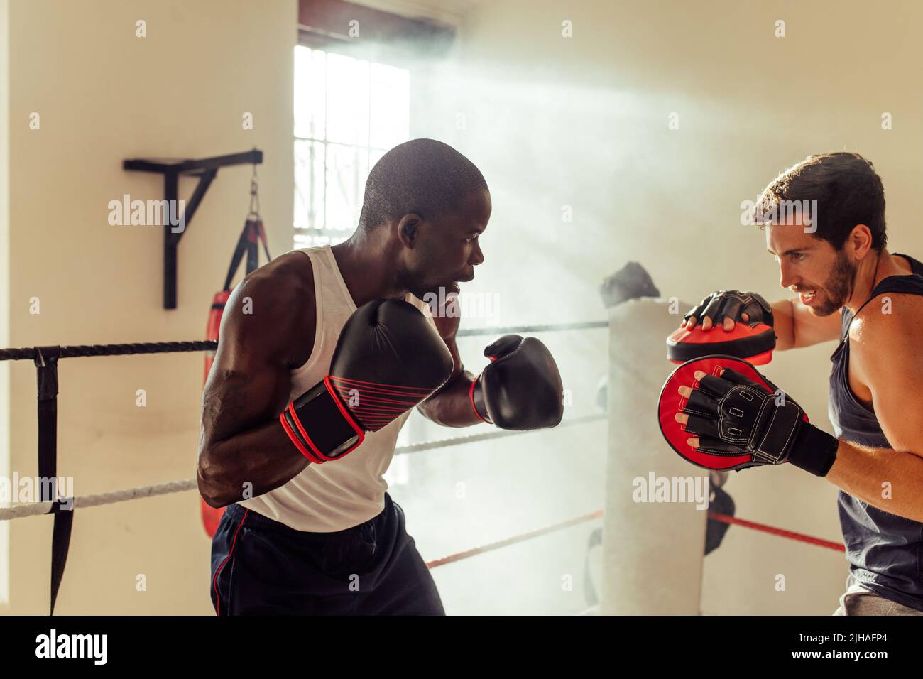 Boxing instructor training a male fighter with focus pads. Young boxing coach teaching a young boxer punching techniques in a gym. Stock Photo