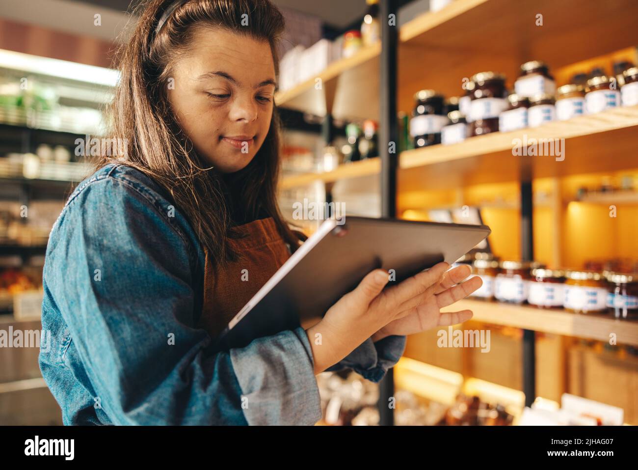 Store employee with Down syndrome taking inventory using a digital tablet. Empowered woman with an intellectual disability working as a shopkeeper in Stock Photo