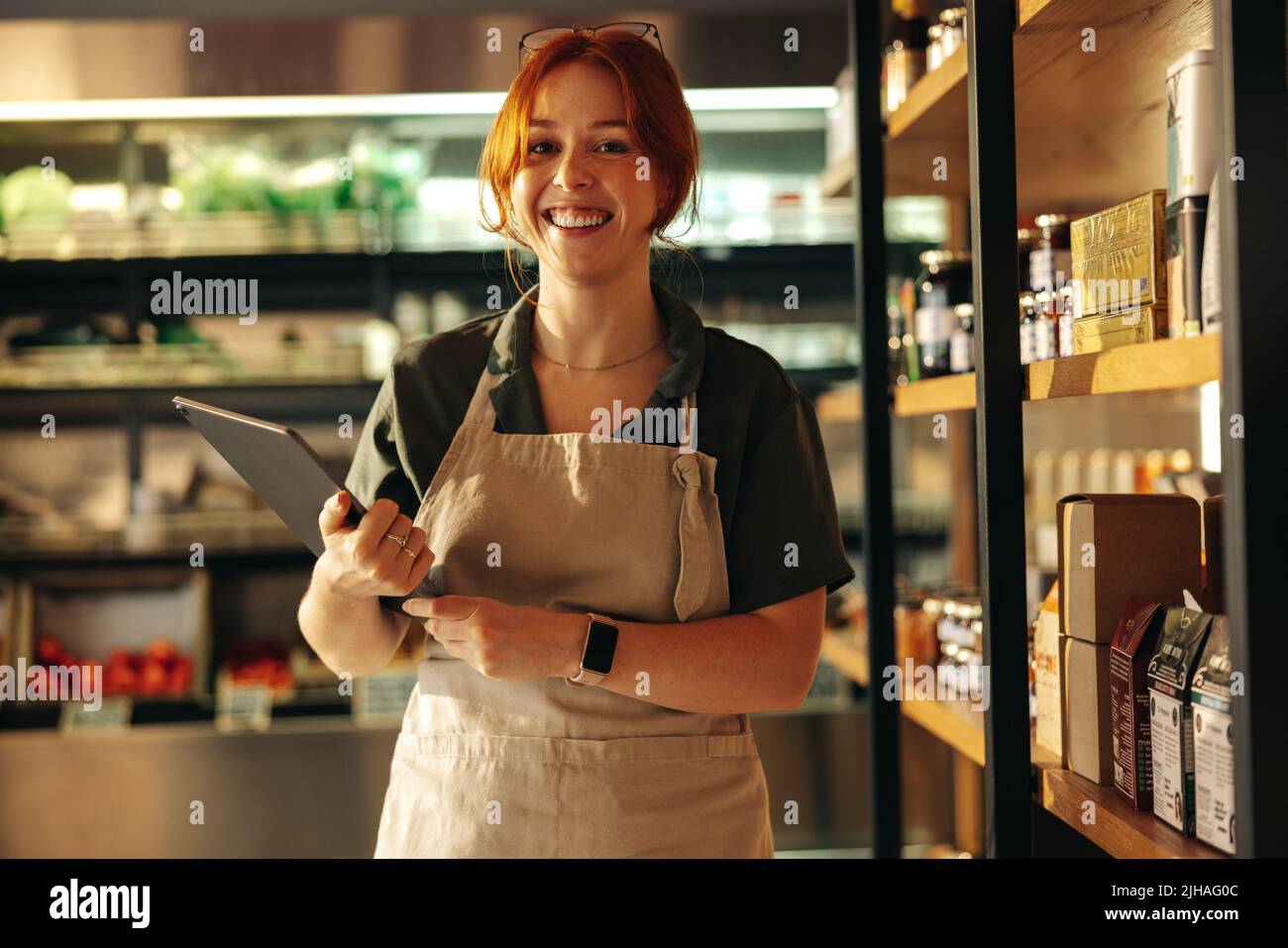 Happy young grocery store owner smiling at the camera while holding a digital tablet. Cheerful female entrepreneur running a successful small business Stock Photo