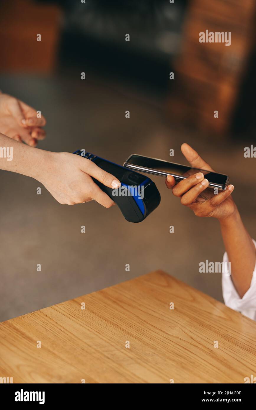 Cafe customer scanning her smartphone on a credit card machine to pay her bill. Unrecognizable woman doing a cashless and contactless transaction usin Stock Photo