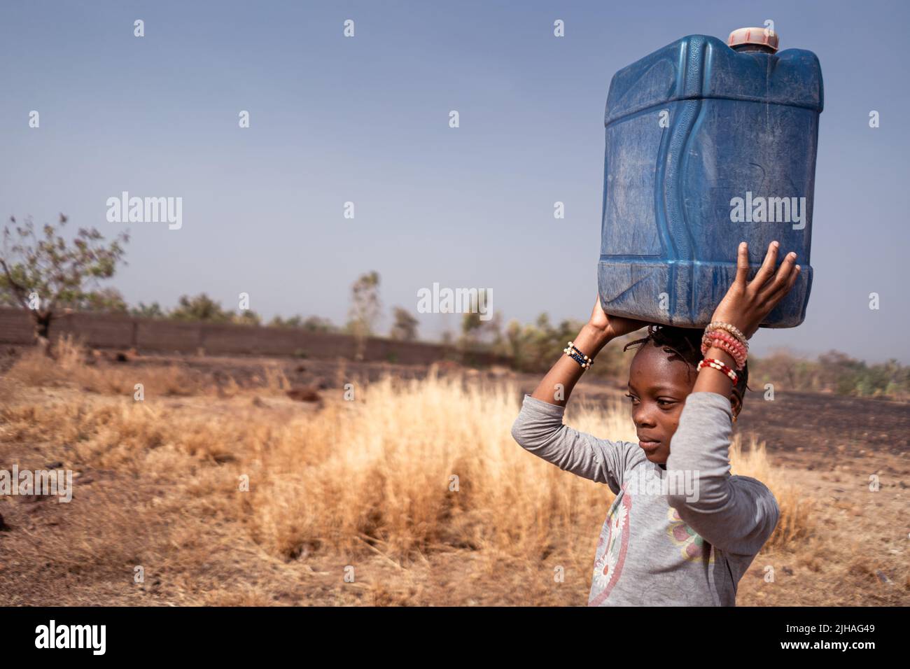 Close up of a serious young African girl carrying a blue water canister on her head Stock Photo