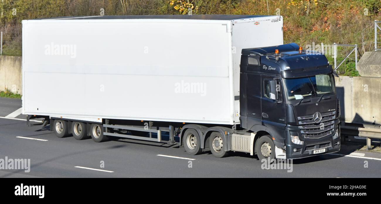 Supply chain transport side front view white unmarked clean rigid body articulated trailer & black hgv Mercedes lorry truck & driver UK motorway road Stock Photo