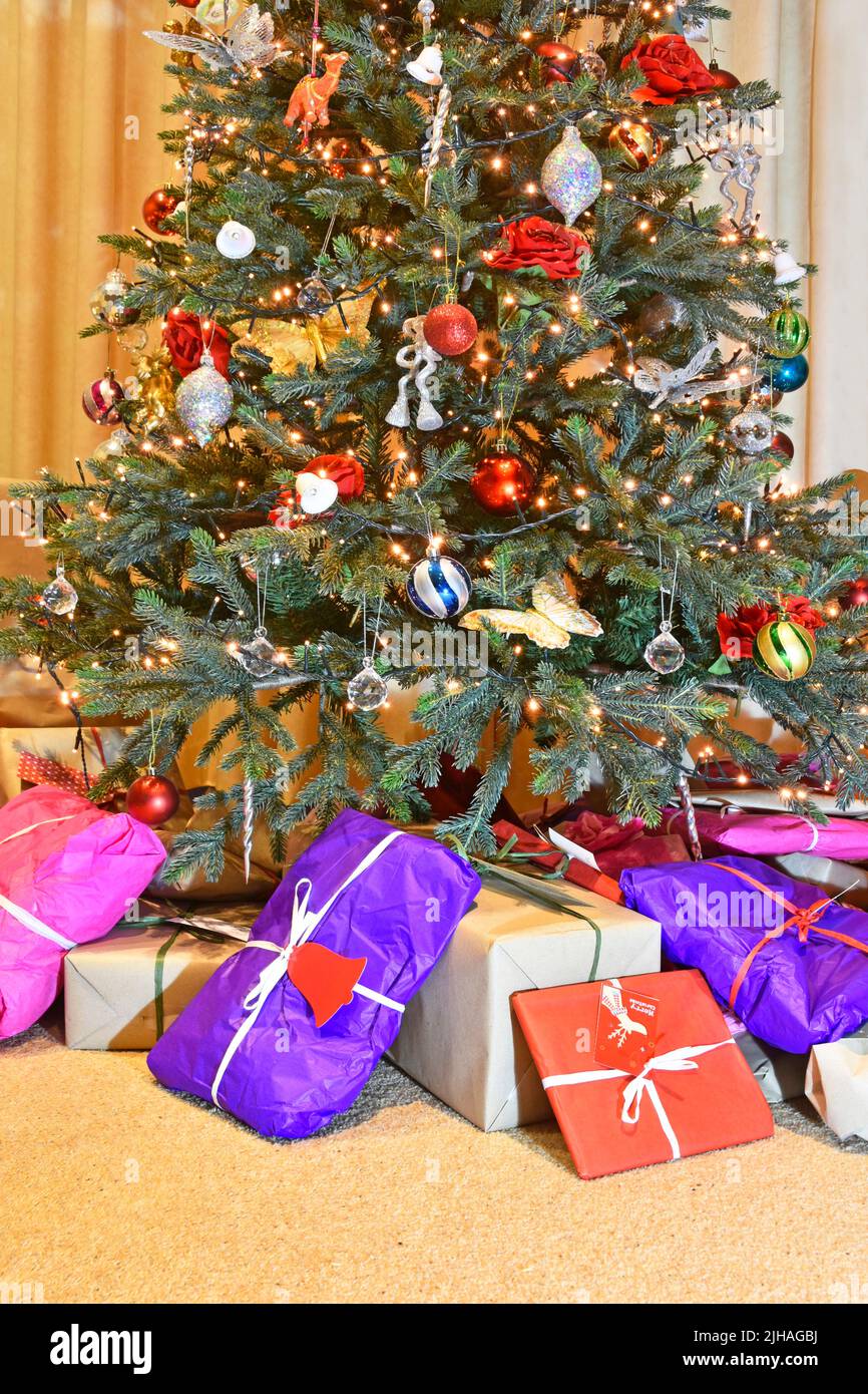 Eco friendly colourful recyclable wrapping paper for Christmas gift & present wrap placed at base of decorated artificial Xmas tree with LED lights UK Stock Photo