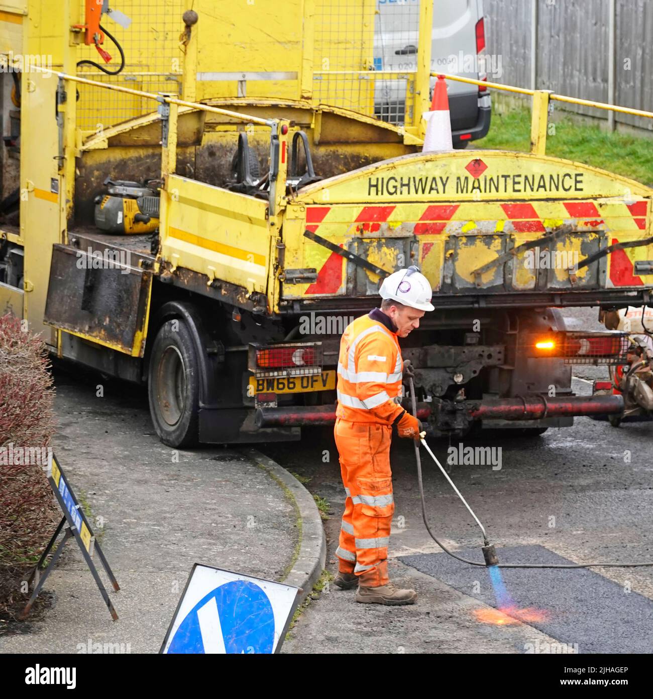 Highway Maintenance man at work on heat sealing tarmac road pothole repair with gas flame torch high visibility yellow tipper lorry truck England UK Stock Photo