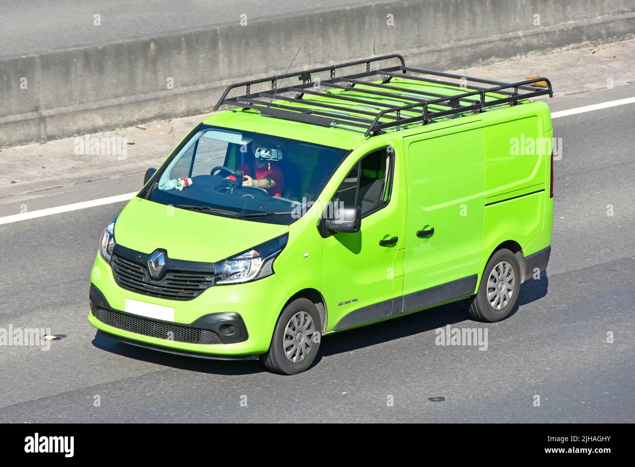 Close up side front & aerial view lime green colour clean unmarked Renault van roof rack driver driving along UK motorway road concrete crash barrier Stock Photo