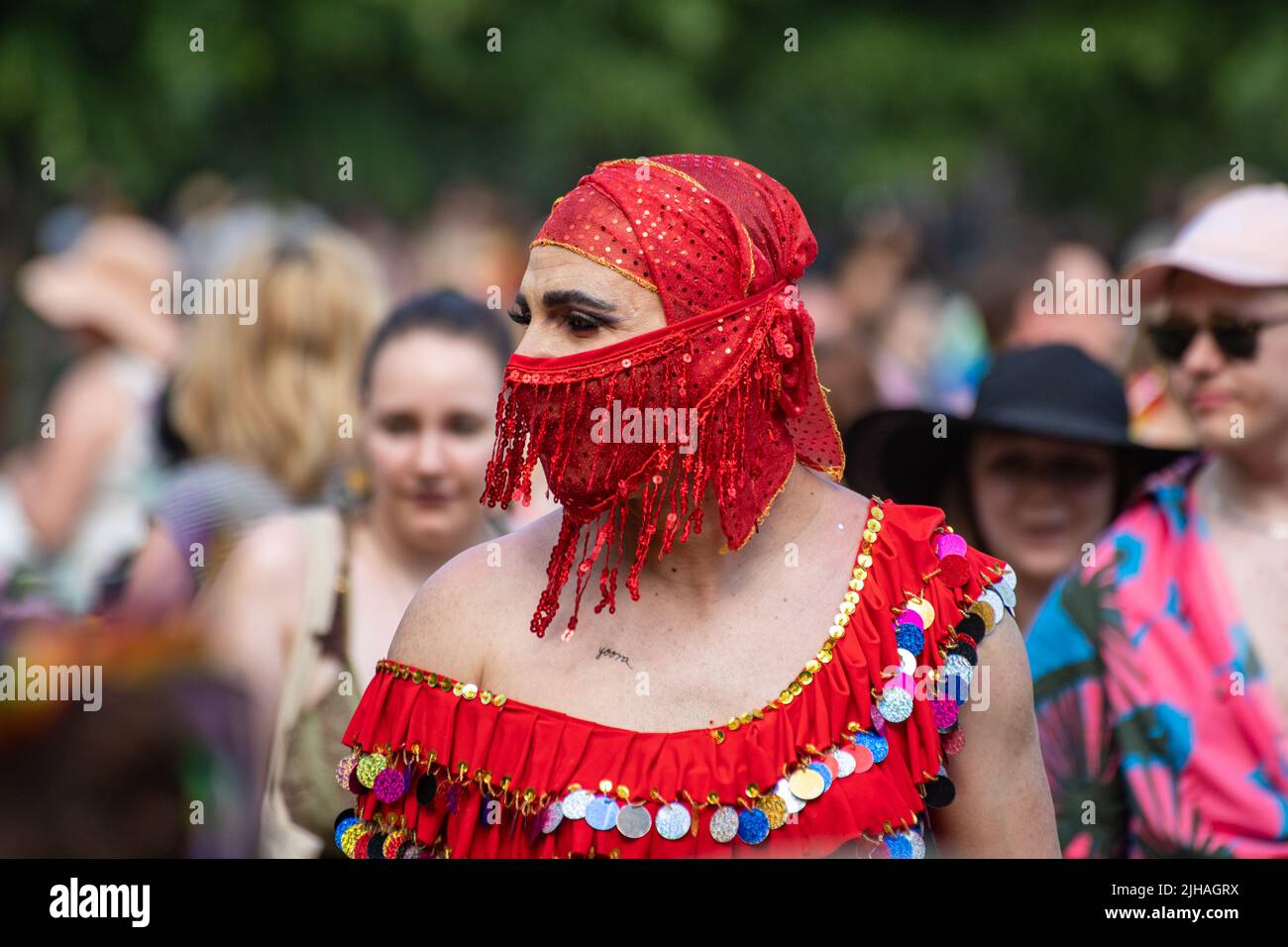 Person wearing belly dancer outfit with red face veil at Helsink Pride 2022 Park Picnic in Kaivopuisto, Helsinki, Finland Stock Photo