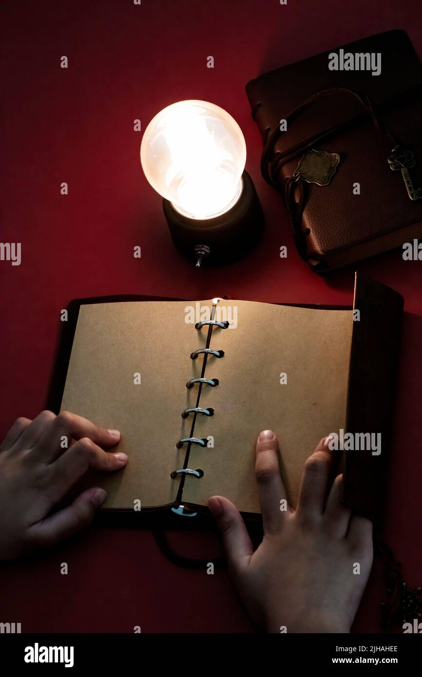 Young man reading on a blank page of a vintage leather book under the low light condition with a yellow, light bulb. Stock Photo