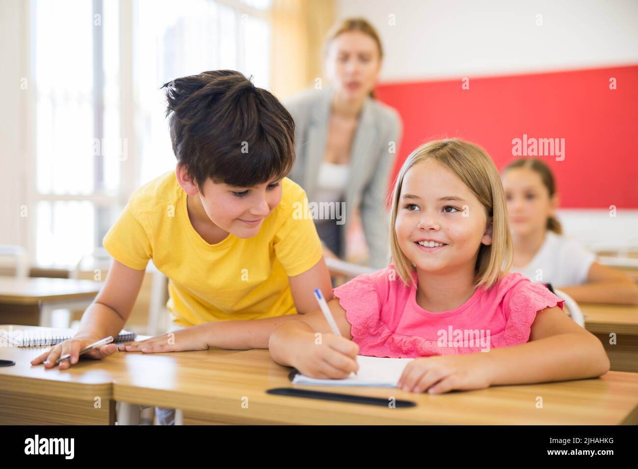 Inquisitive preteen boy peeking at workbook of cute smiling girl in class Stock Photo