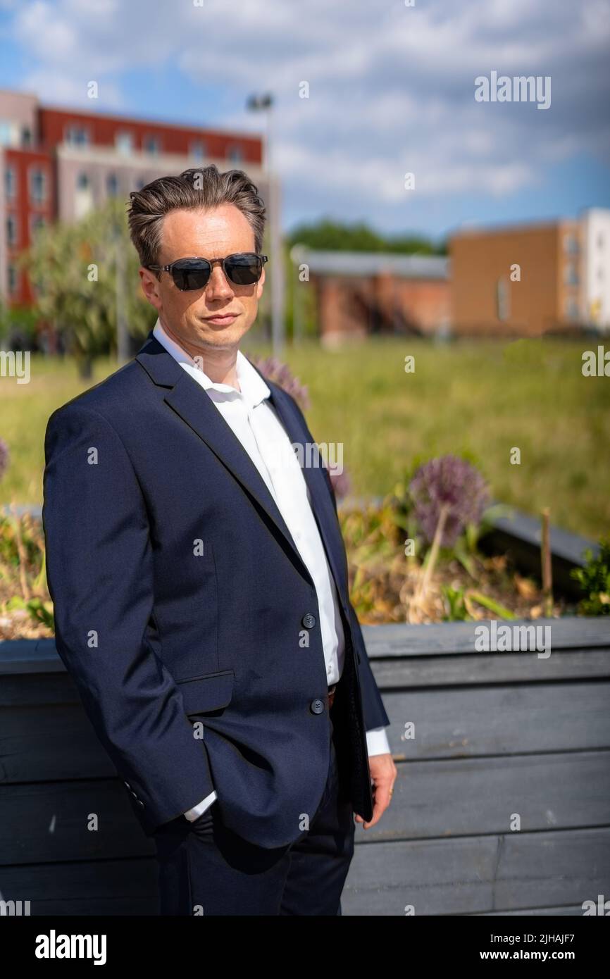 A handsome businessman in a casual dark blue suit in front of a residential area Stock Photo