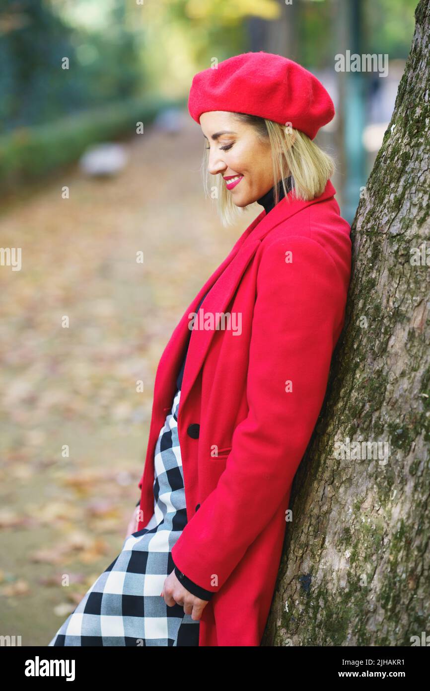 Smiling woman in red outfit and skirt leaning on tree Stock Photo