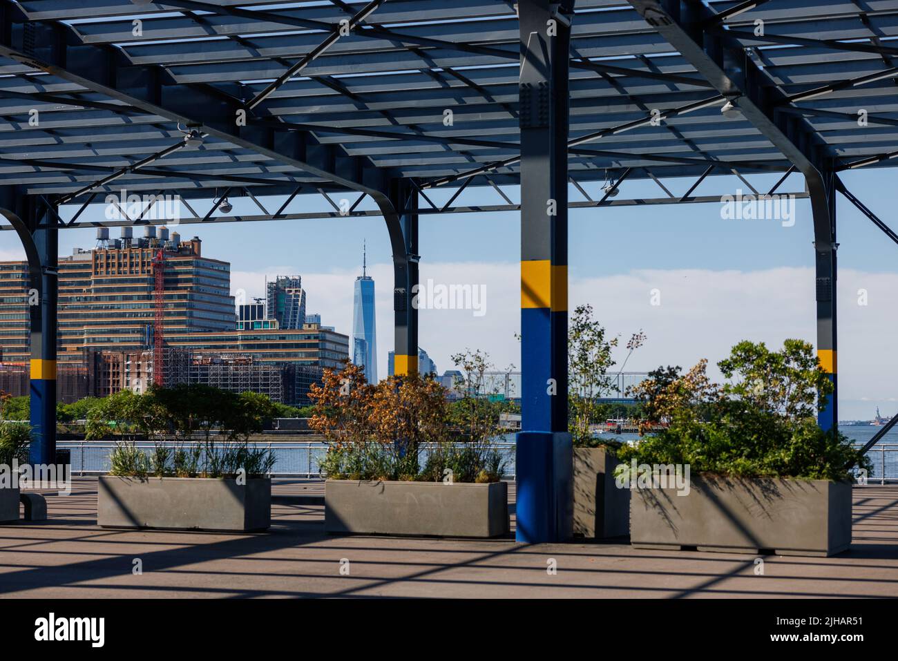 The garden under shade with cityscape and water in background. Plants in concrete pots under canopy Stock Photo