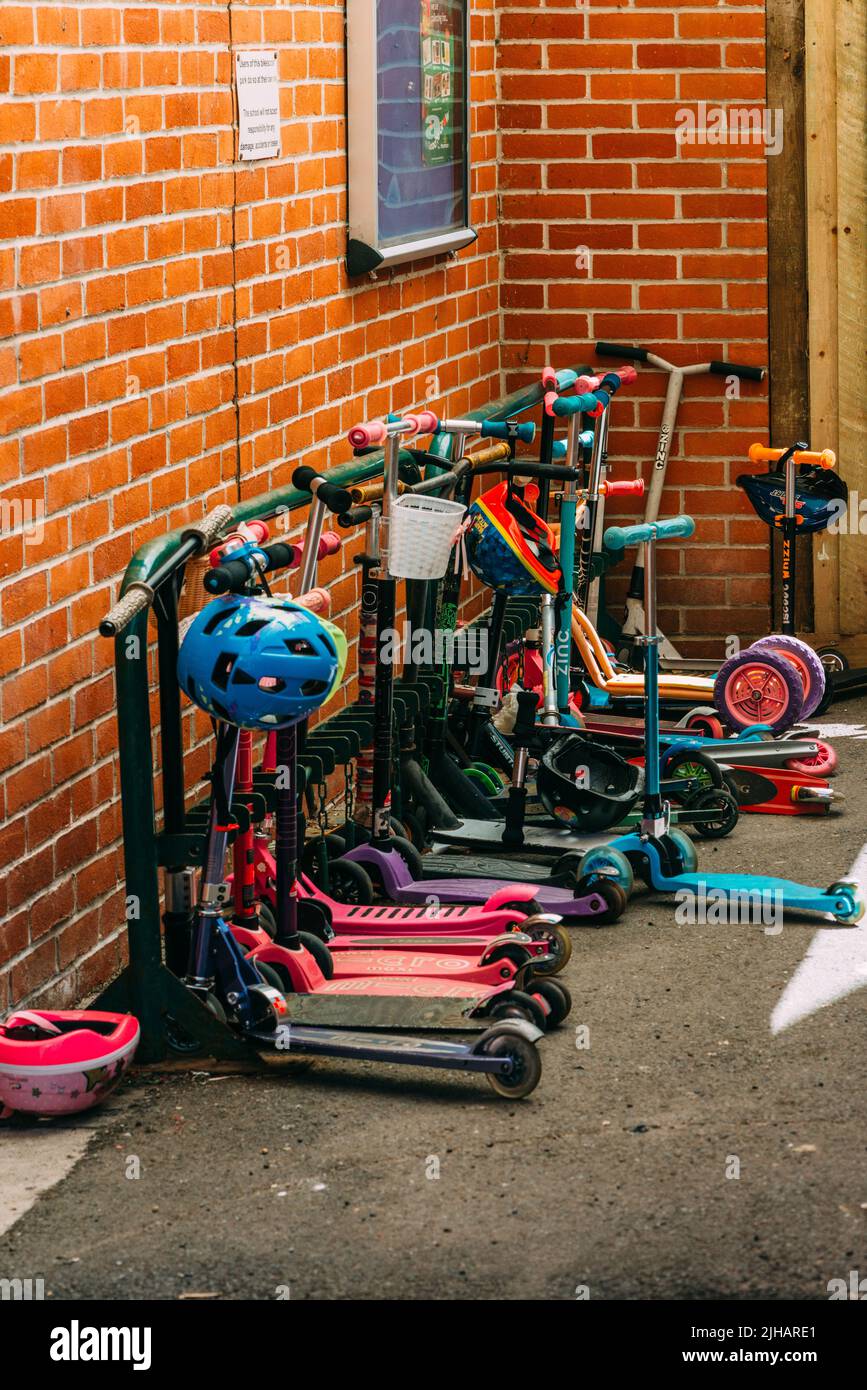 Children's scooters of different colours parked outside a school in Canterbury, UK Stock Photo