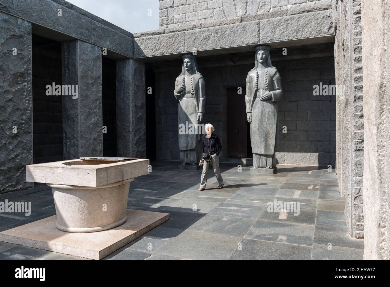 Elderly woman walking out of the Mausoleum of Negos of which the entrance is supported by 2 caryatids, sculpted female Montenegrin figures.Montenegro. Stock Photo