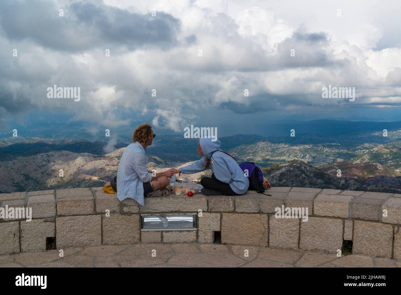Young couple having lunch on the edge of the Guvno lookout point of the Mausoleum og Njegos. Montenegro Stock Photo