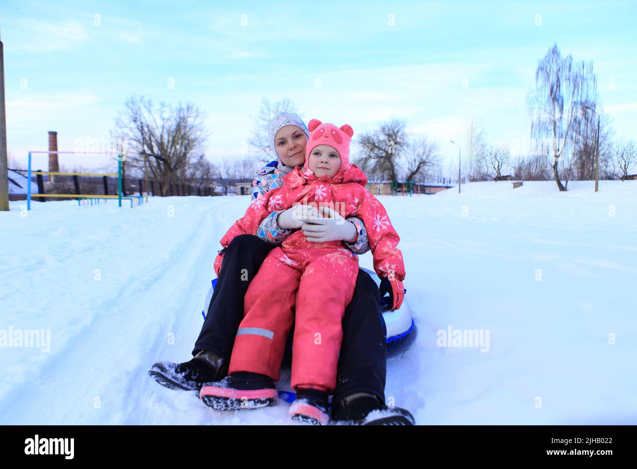 Mom and daughter ride a tubing in winter. The family spends time outside in winter. Sled games Stock Photo