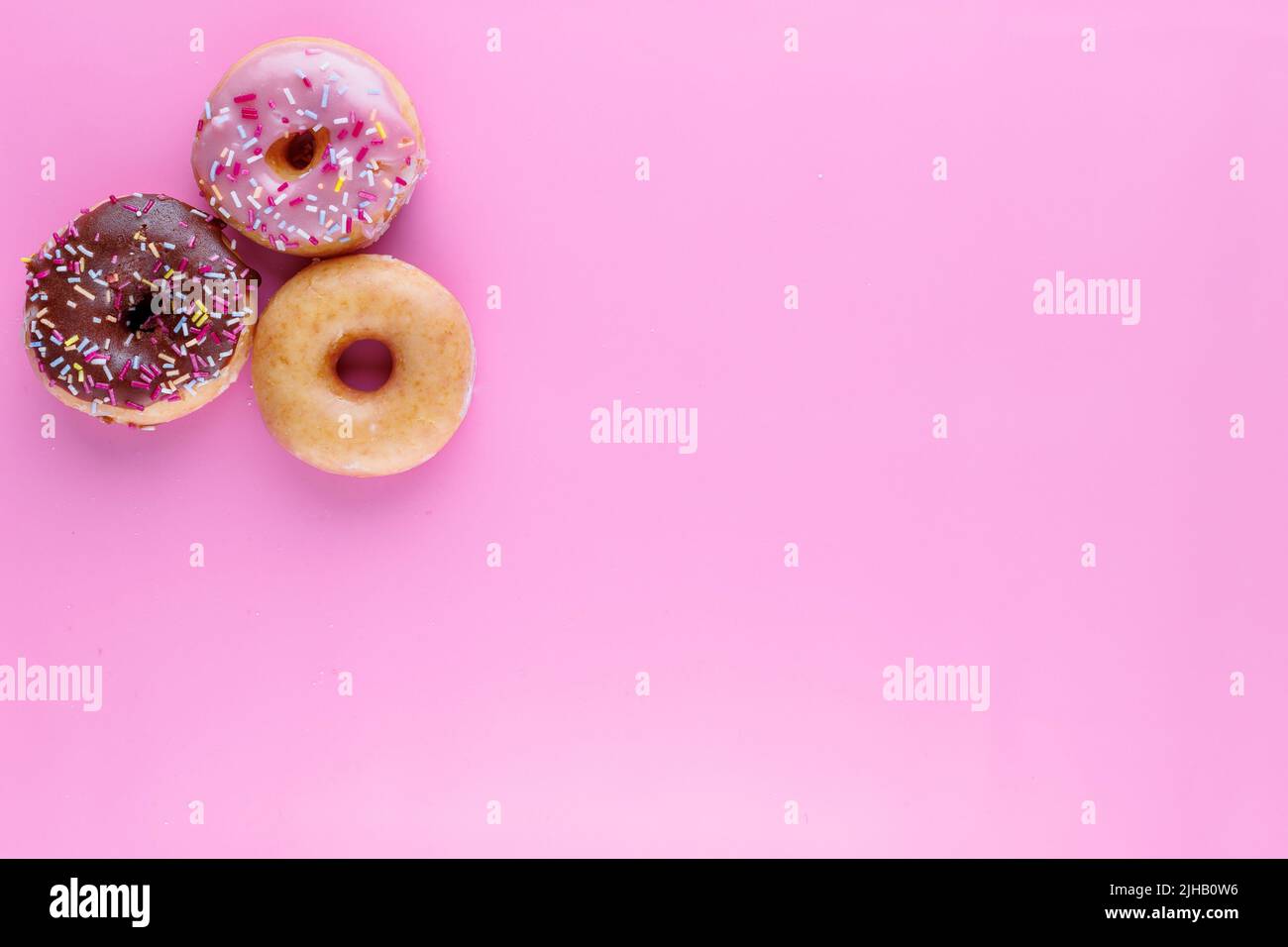 Sugar icing glazed doughnuts, including a chocolate sprinkle-topped variety, arranged in a flat lay on a solid background with negative space. Stock Photo