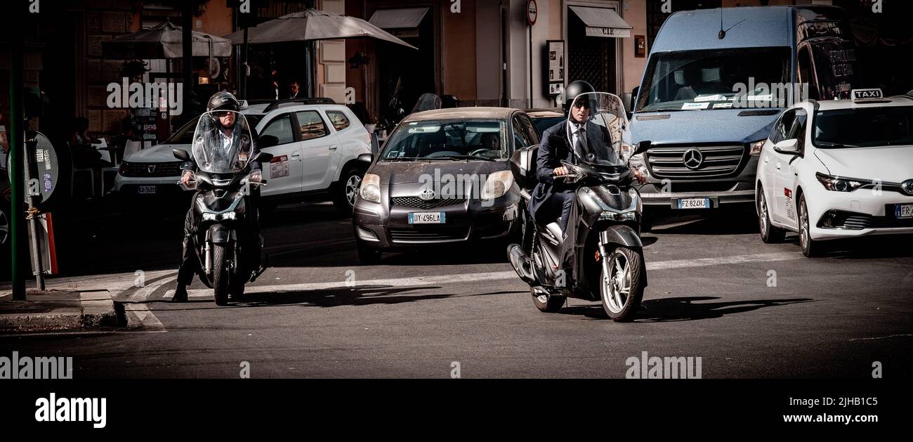 Rome, Italy - June 6, 2022: Businessman on motorbike waits in front of traffic on busy Rome street. Stock Photo