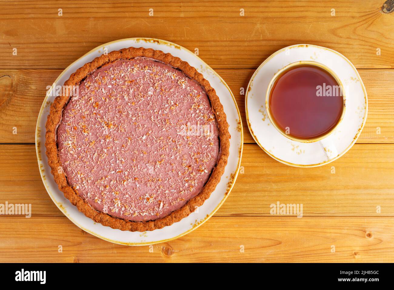 Homemade raspberry and banana pie and cup of tea on wooden table. Top view. Stock Photo