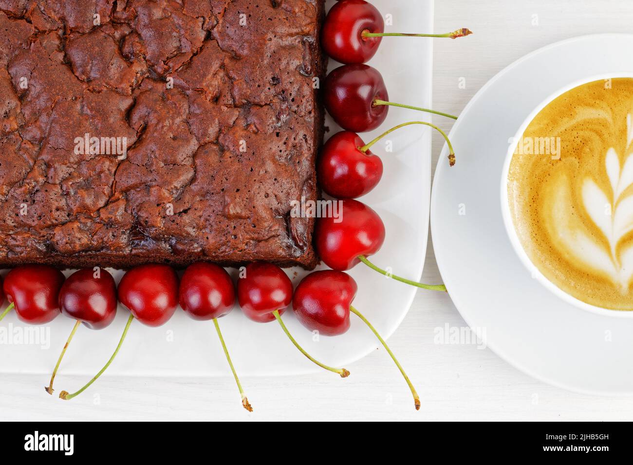 Closeup homemade brownie with cherry and cup of coffee cappuccino on white wooden table. Top view. Stock Photo
