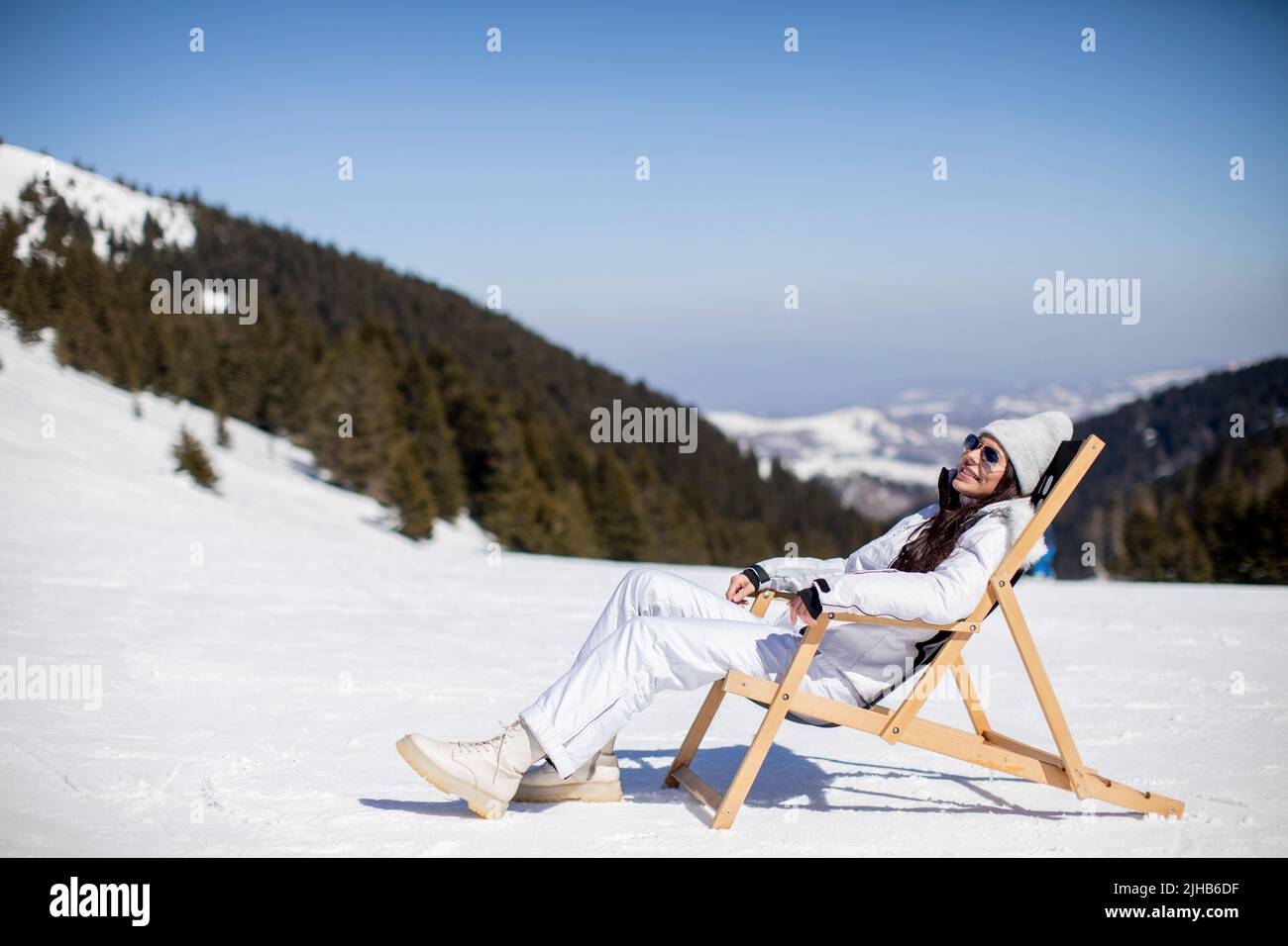 Pretty young woman sitting at deck chair on ski track at the snowy mountain Stock Photo