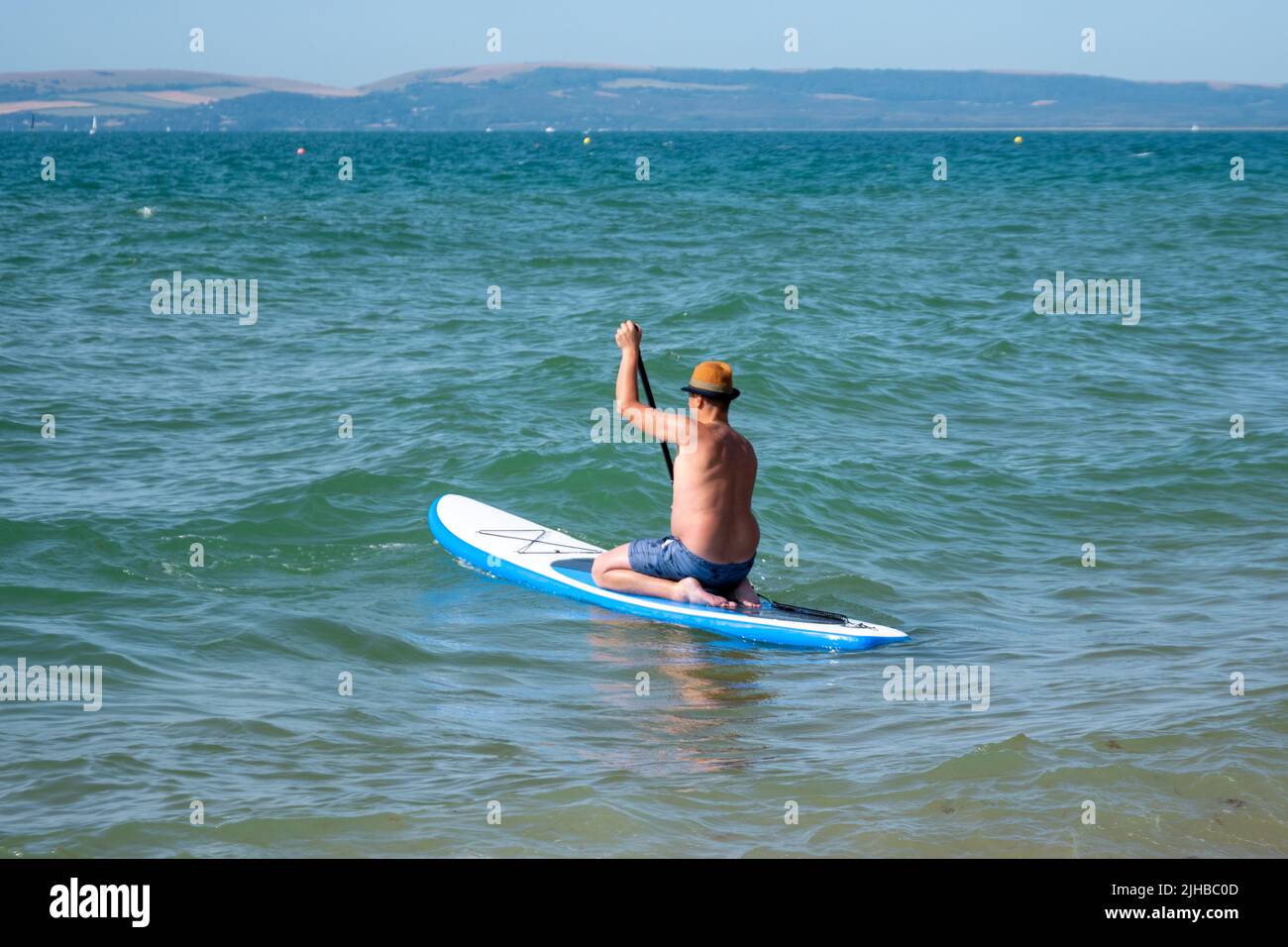 Boscombe Beach, Bournemouth, Dorset, England, UK, 17th July 2022, Weather. Record breaking heatwave moves in across the south coast and an amber warning is in place from the Met Office for heat. A paddleboarder in a pork pie hat paddles out to sea. Credit: Paul Biggins/Alamy Live News Stock Photo