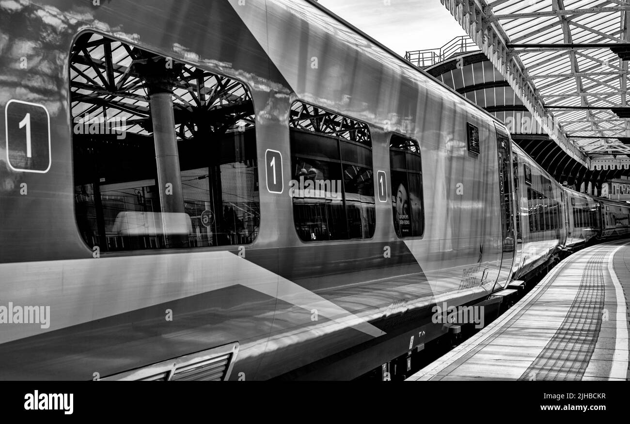 A close-up of railway carriages resting beneath a historic canopy. The awning is reflected in the carriage windows. Stock Photo