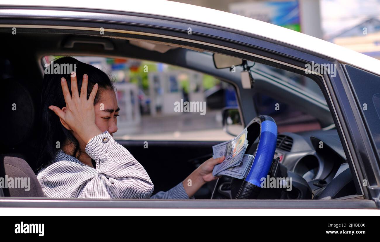 Desperate beautiful Asian woman holds cash dollar bills sitting inside