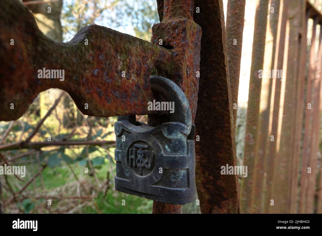 A rusty old padlock on a rusting iron gate. A padlock manufactured by Henry, William and Thomas Vaughan, famous locksmiths of Willenhall in the UK in Stock Photo