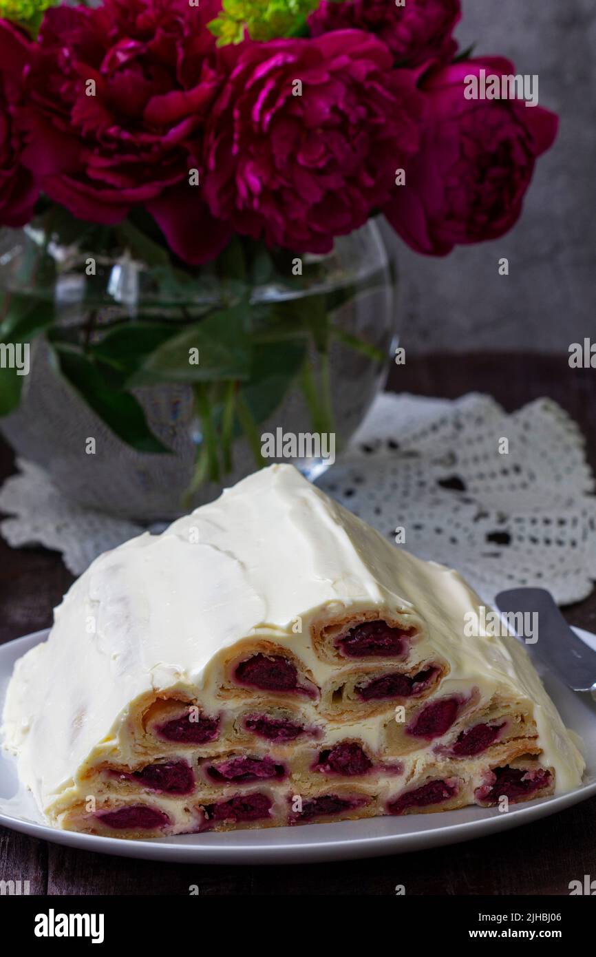 Cake Monastic hut with cherry filling and sour cream, a bouquet of peonies on a wooden table. Stock Photo